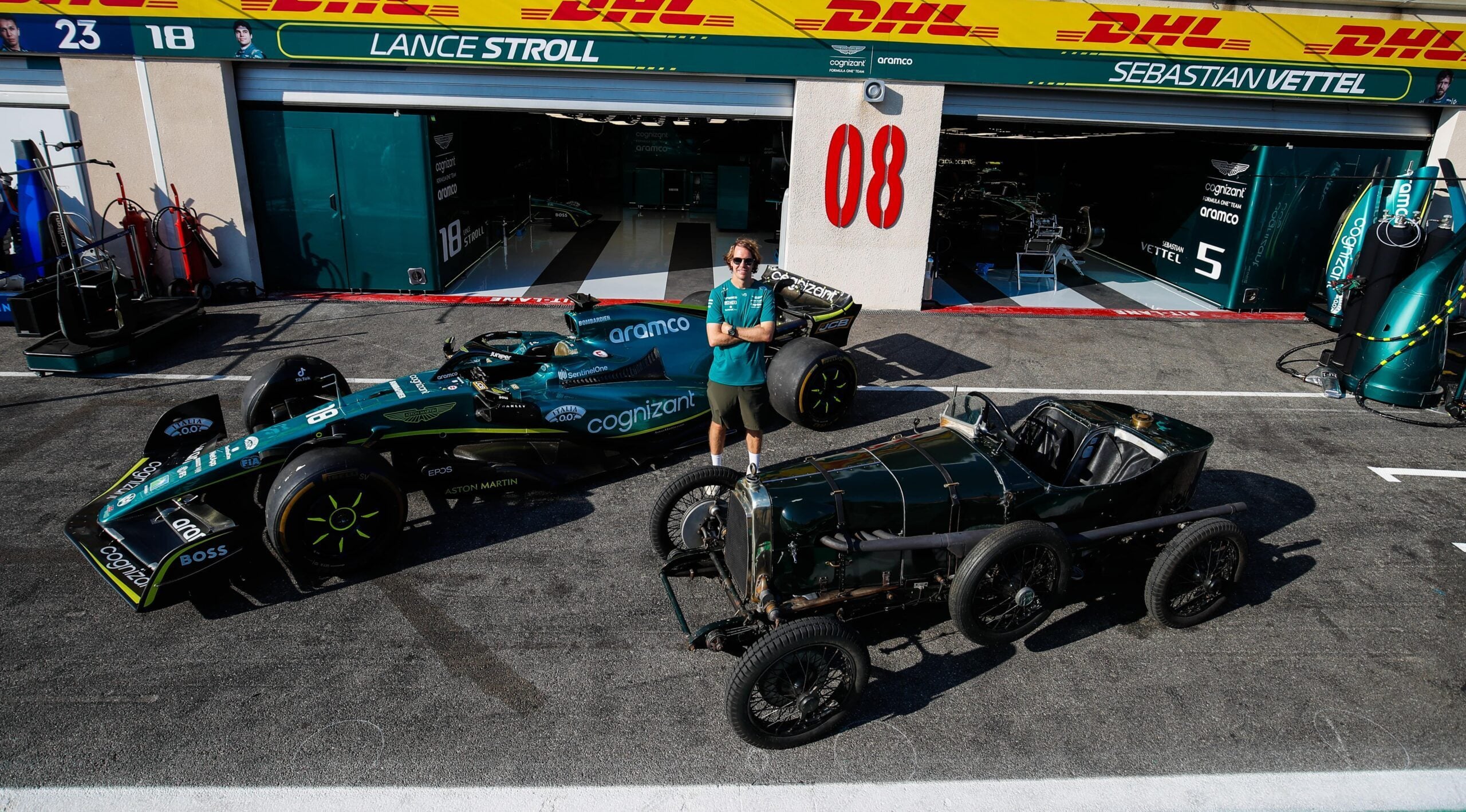 Sebastian Vettel standing between AMR22 Formula 1 car and 1922 Aston Martin TT1 Green Pea
