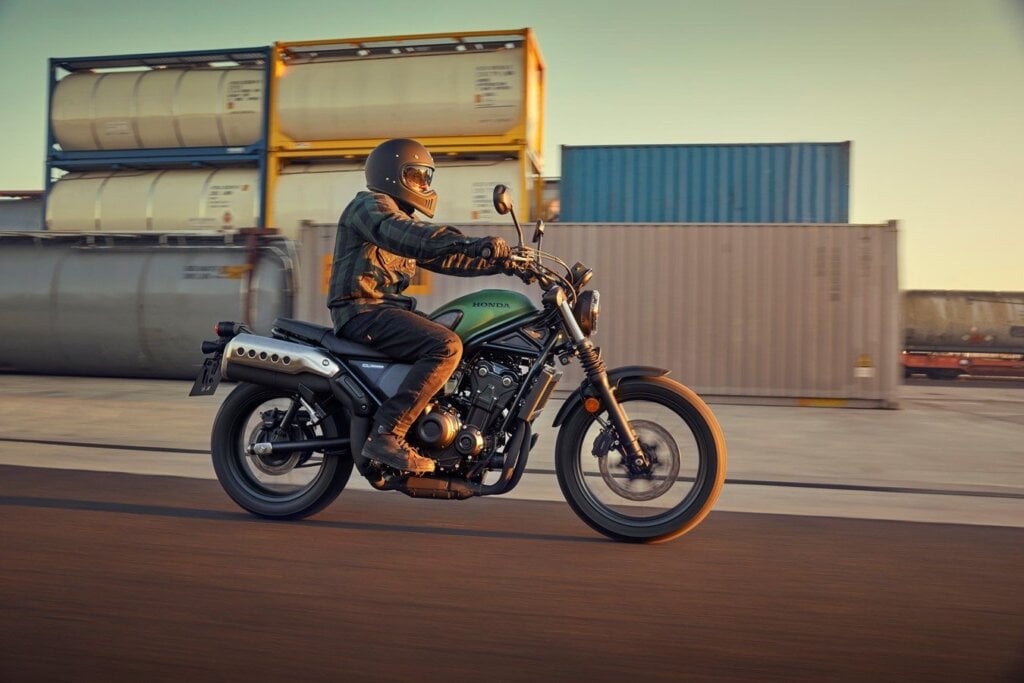 Honda CL500 riding past containers