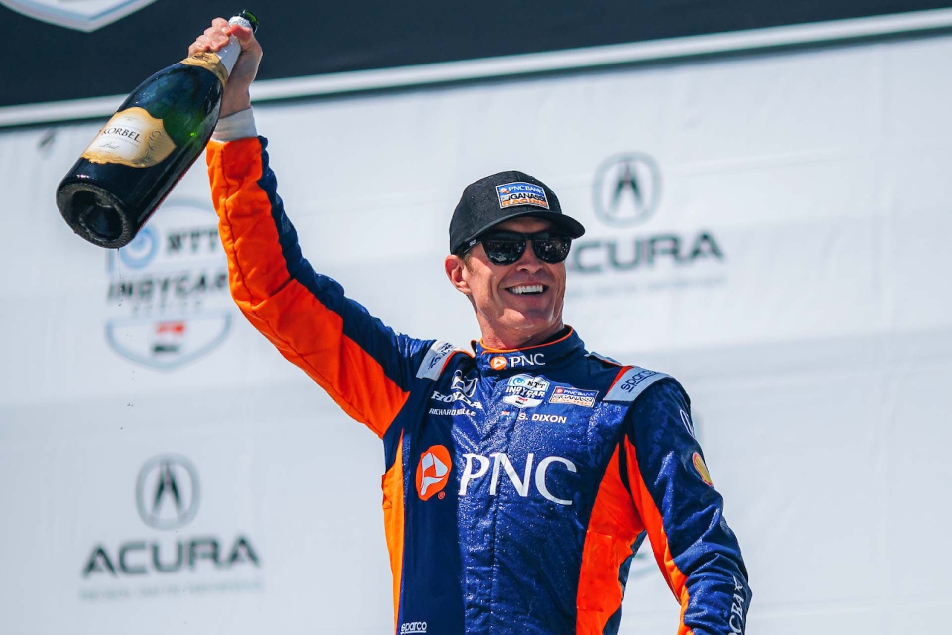 Scott Dixon holding up a bottle of Champagne and smiling