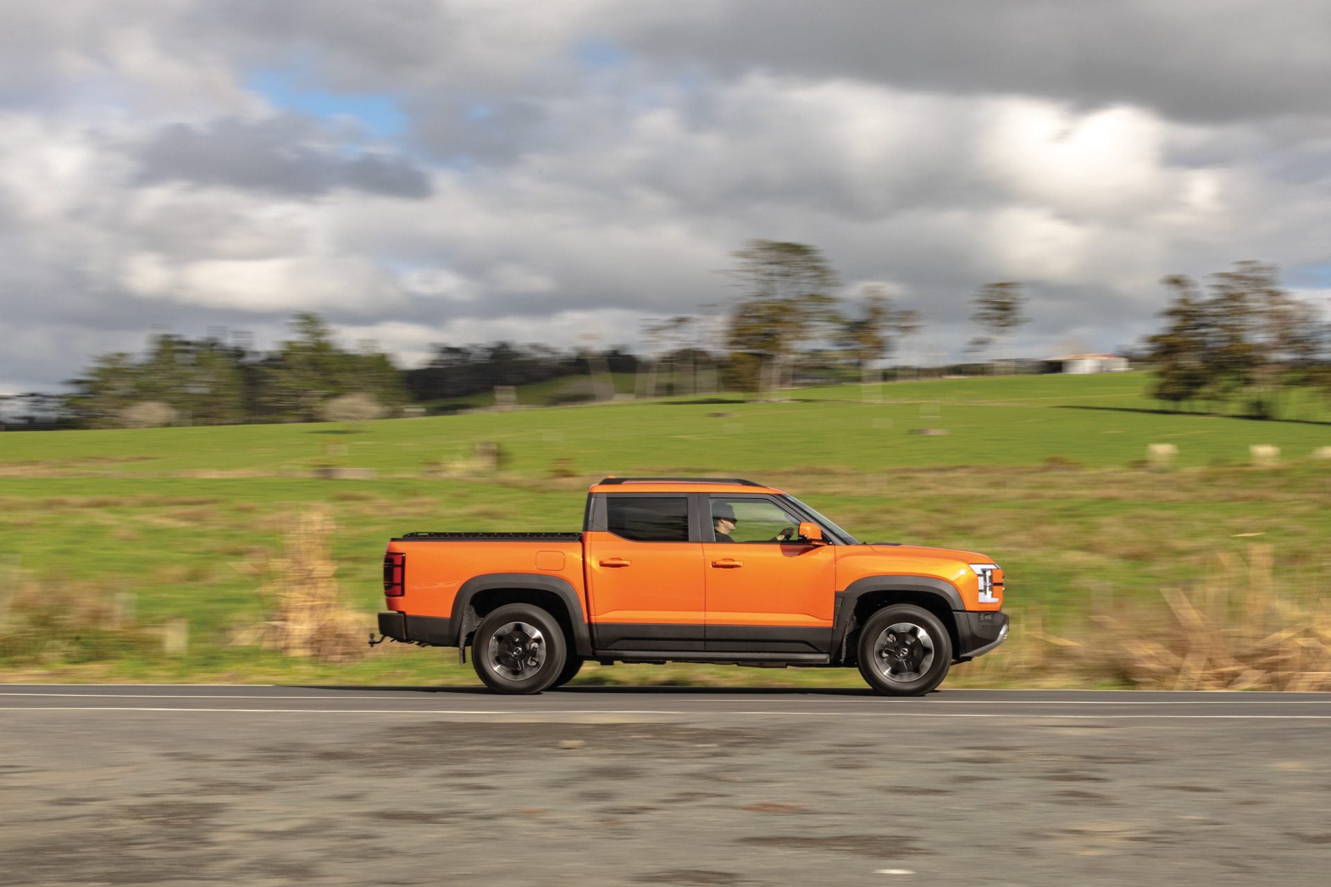 Orange BYD Shark 6 plug-in hybrid ute side view on a New Zealand rural road