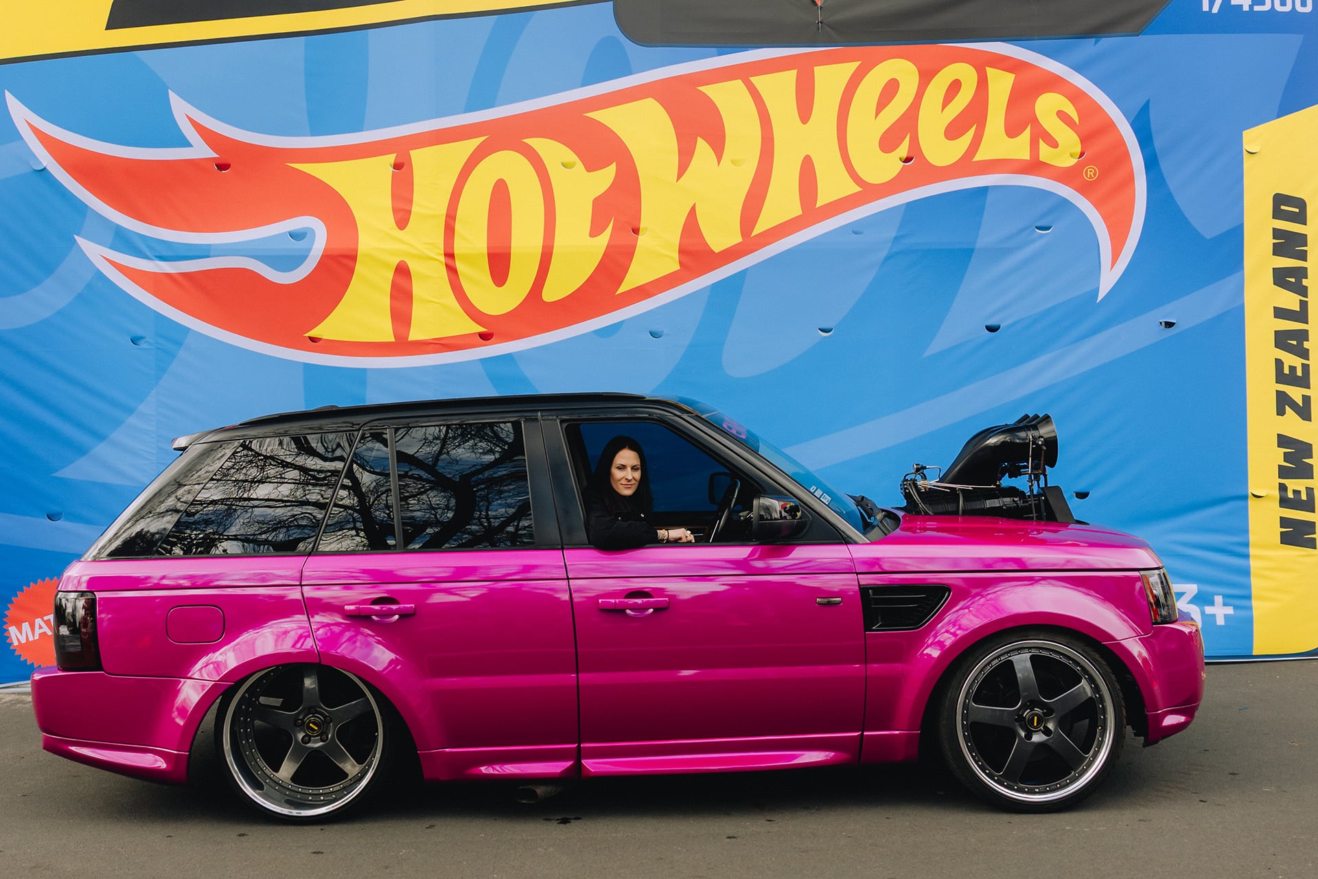 A Range Rover Sport in pink in front of a blue hot wheels sign
