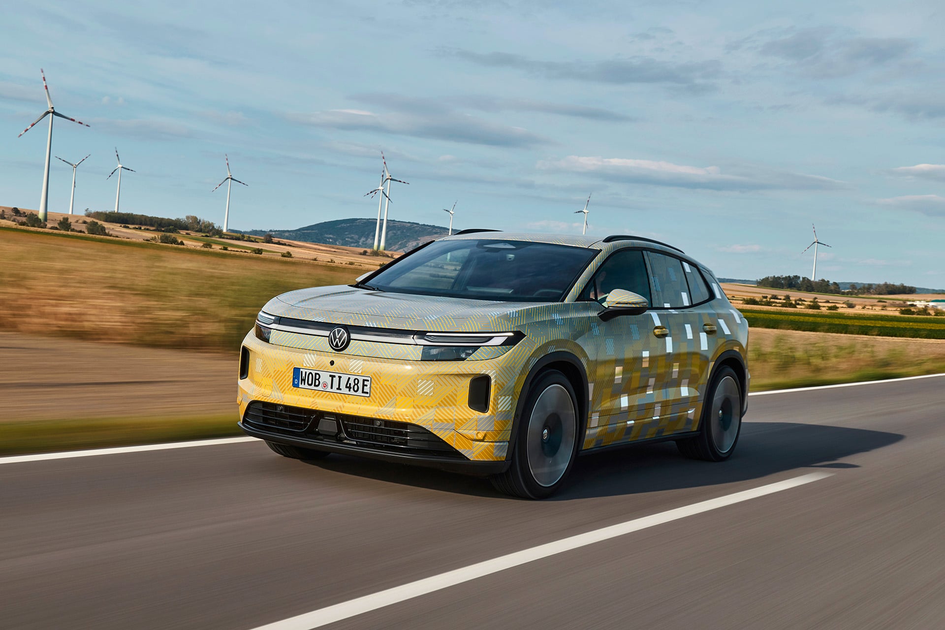 electric Tiguan in yellow on a road in front of wind turbines