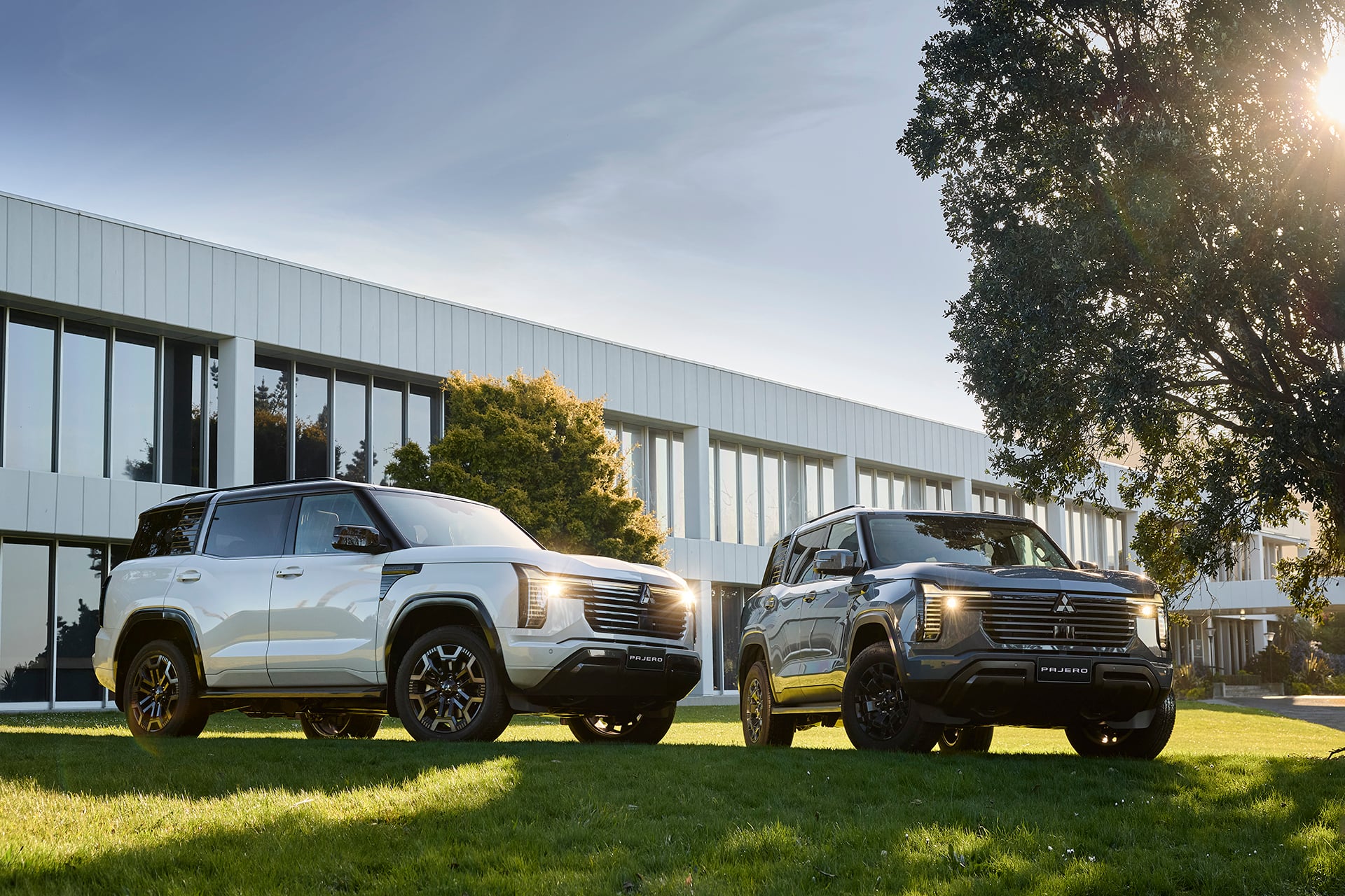 pajeros in white and grey on grass. in front of building