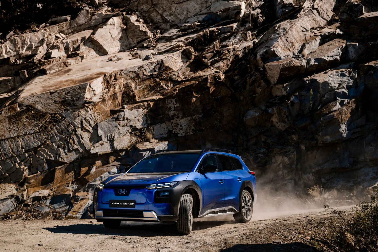 Blue Subaru Trailseeker AWD Touring driving past a rock face on a dusty road