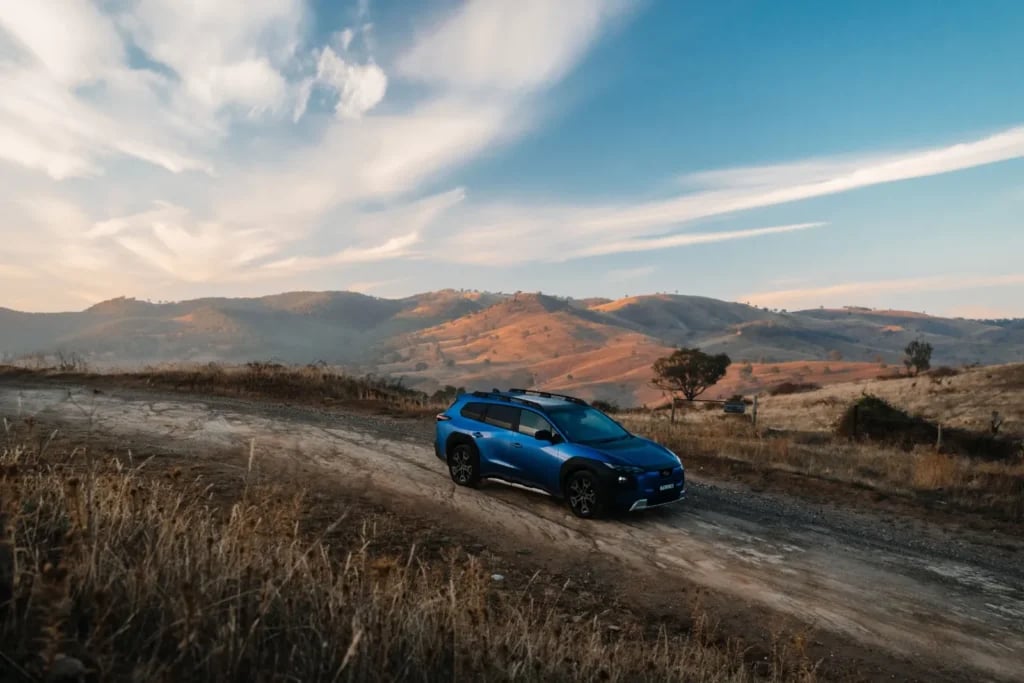 Blue Subaru Trailseeker driving on a gravel road through dry hills