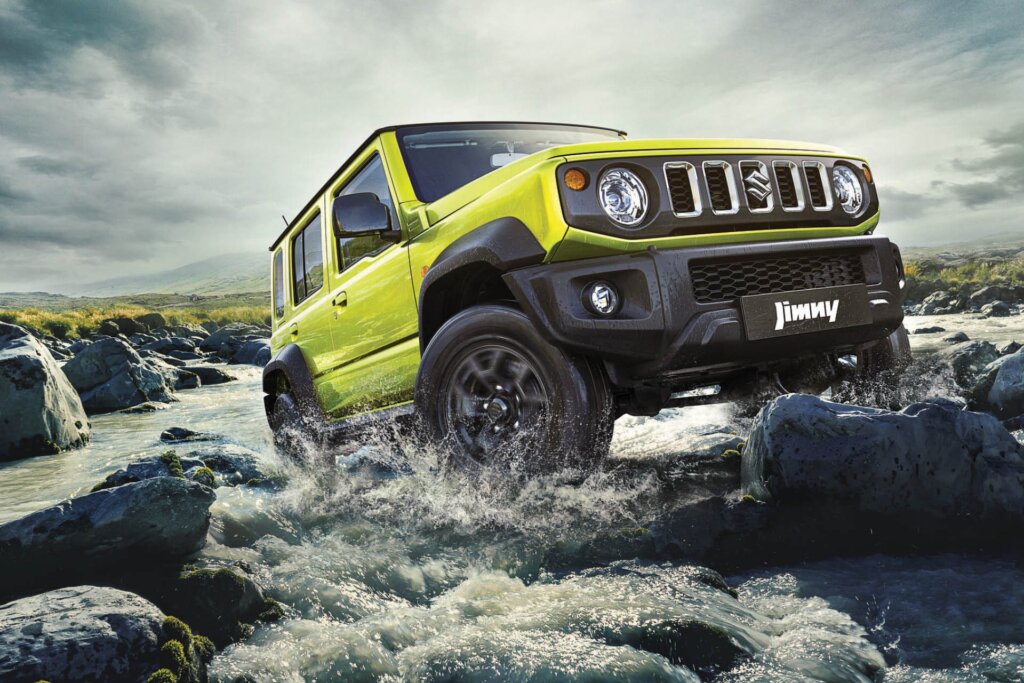 Five-door Suzuki Jimny driving over rocks in river