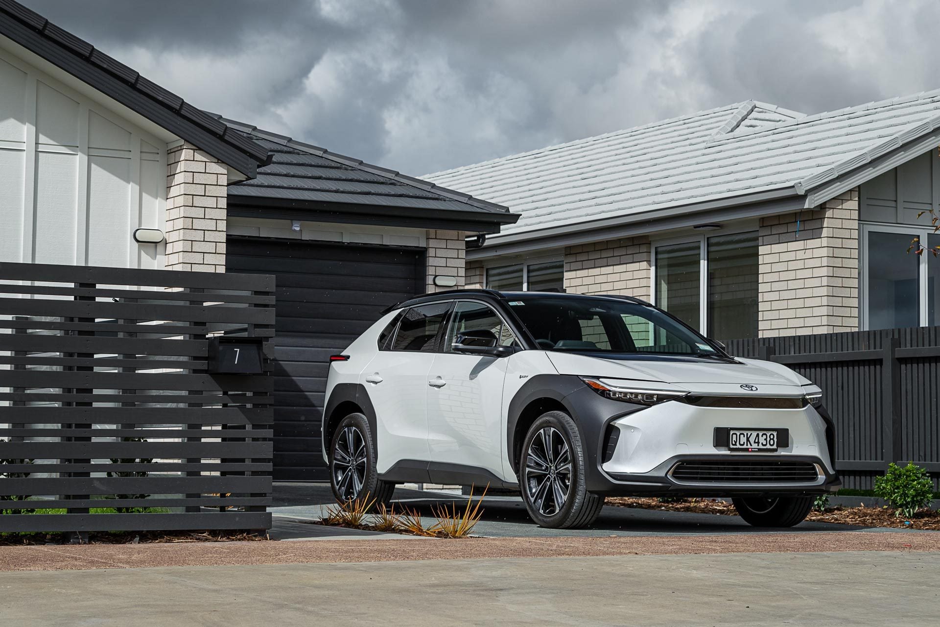 Toyota bZ4X Pure, in white and black, in front of a new house