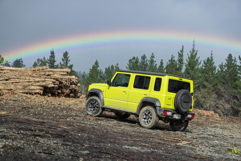 2024 Suzuki Jimny 5-door with logs and rainbow behind car