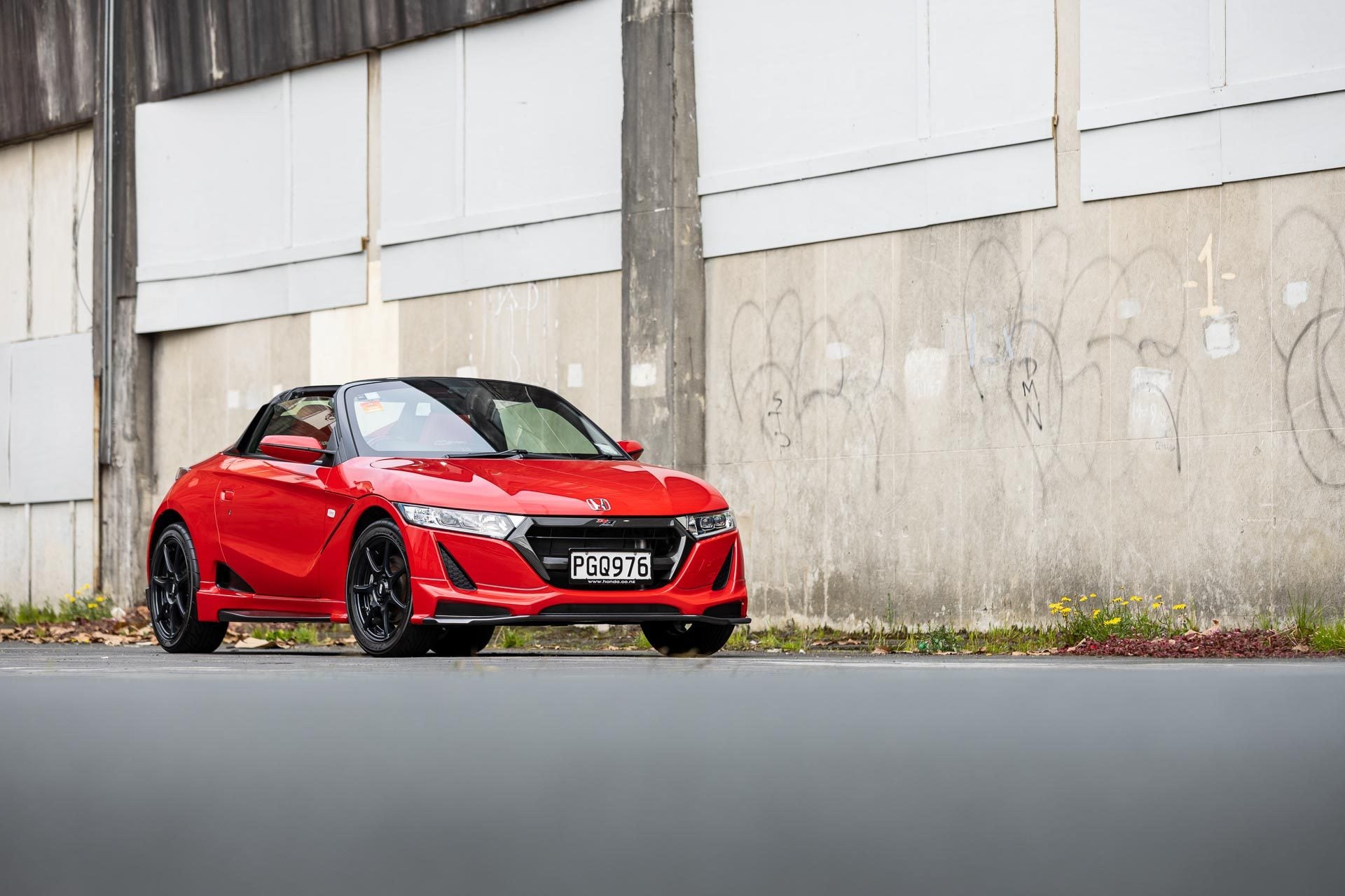 Honda S660 Mugen in red, parked in front of an urban wall