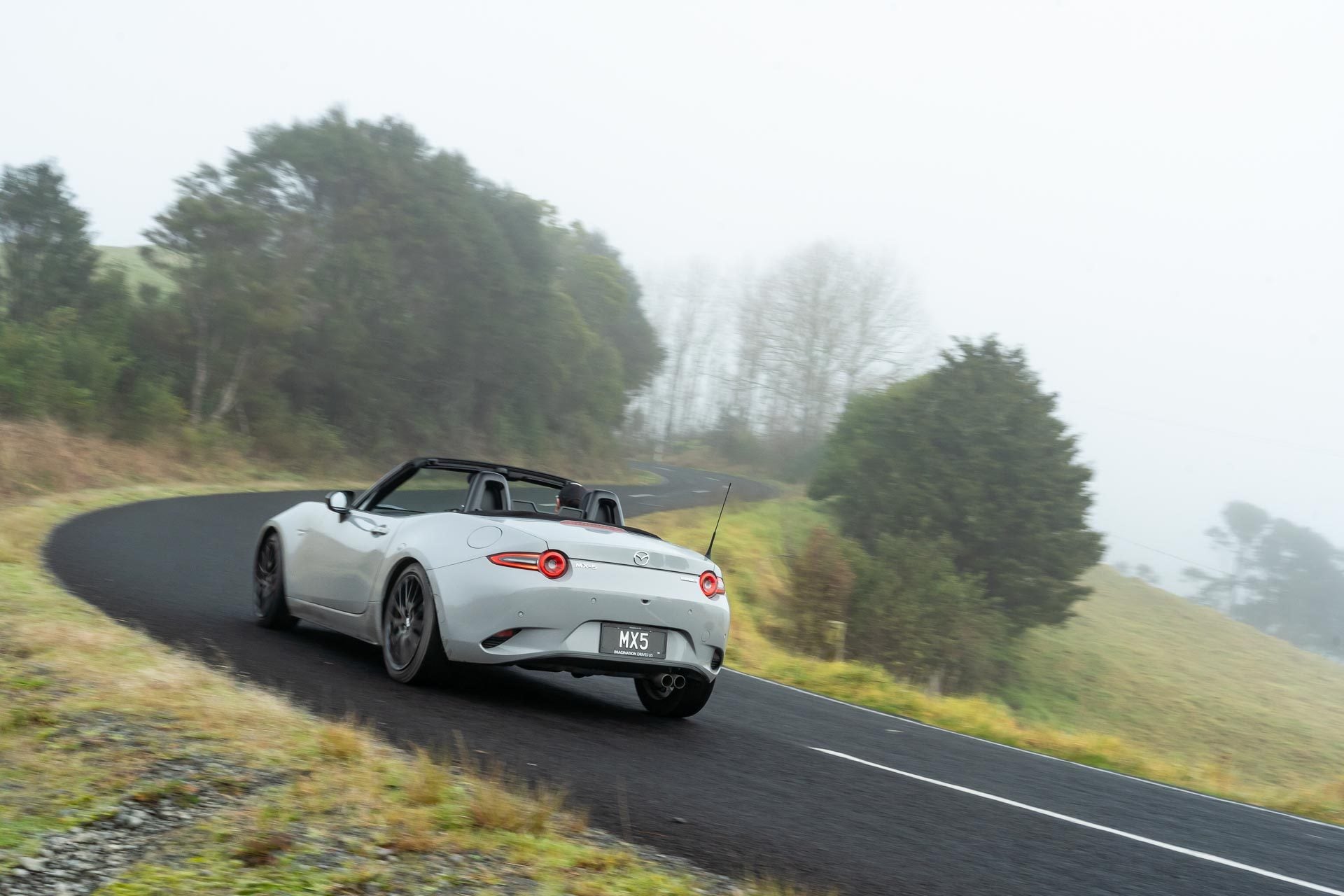 Mazda MX-5 cornering at pace, shown from the rear, on a foggy road