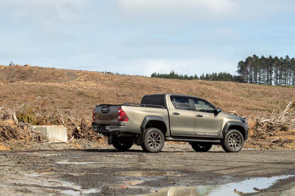 2024 Toyota Hilux SR5 Cruiser Hybrid rear side profile shot, parked on gravel and mud