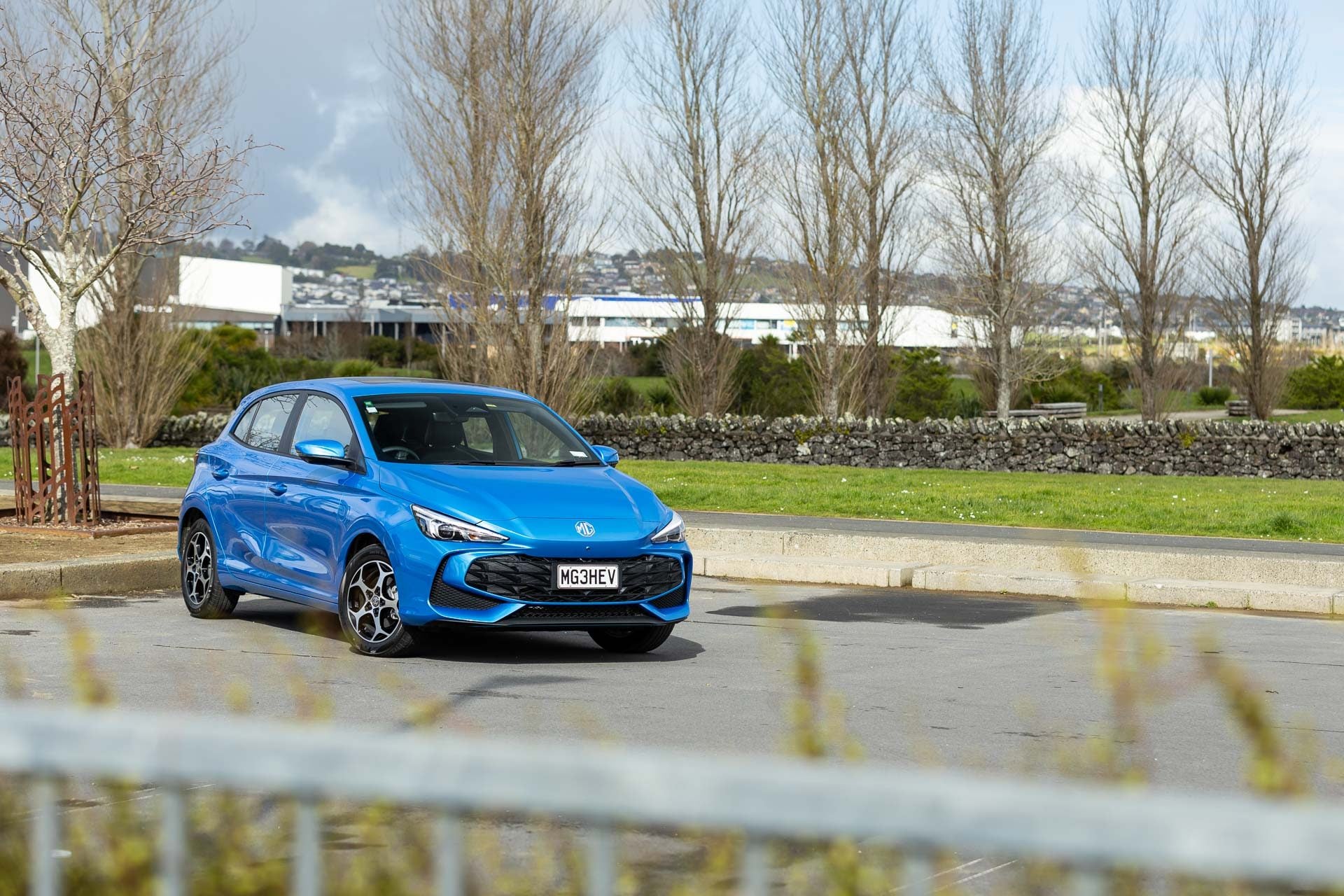 MG MG3 Hybrid Essence, parked in a carpark with trees behind, and a fence in front