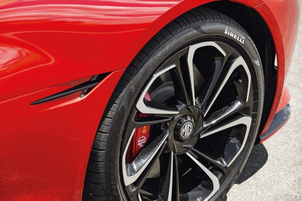 Close-up of the front wheel of a red MG Cyberster, featuring a black and silver alloy rim with the MG logo, red brake caliper with MG and Brembo branding, and a Pirelli tire