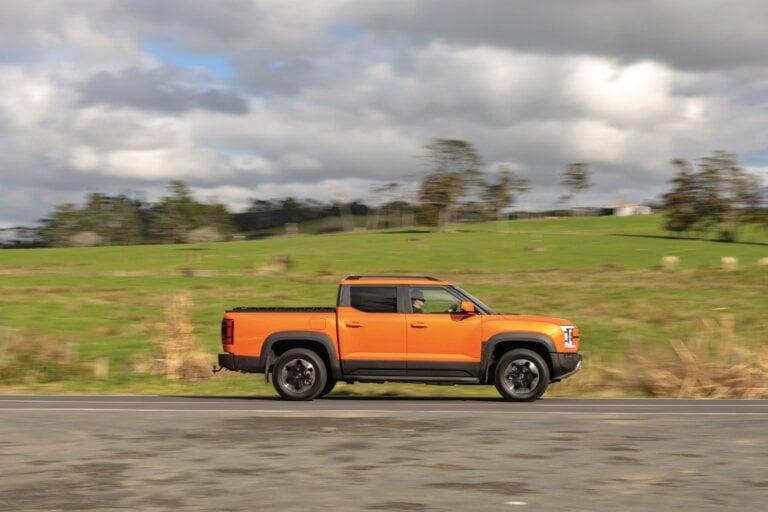 Orange BYD Shark 6 plug-in hybrid ute side view on a New Zealand rural road