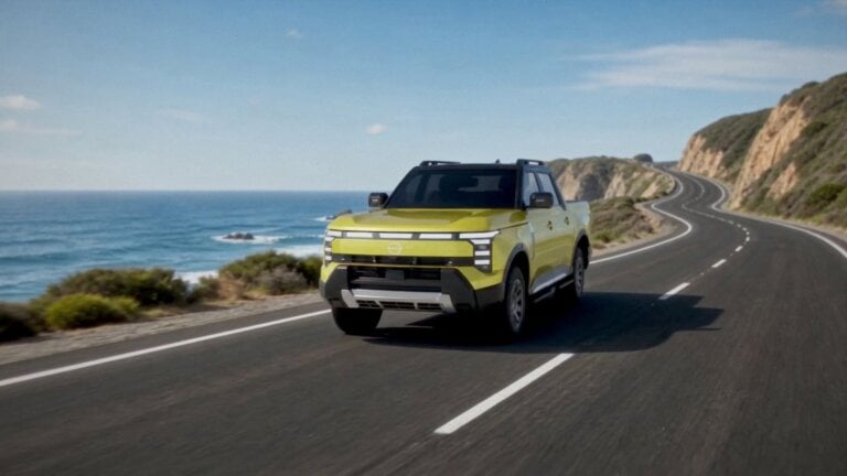 Yellow Nissan Navara Pro PHEV ute driving on a coastal road, front view